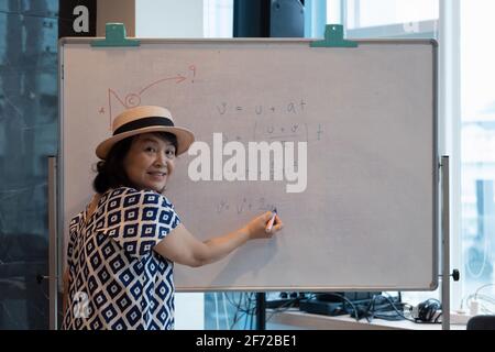 Moderne Bildung aus der Ferne. Fröhliche ältere Frau zeigt auf das Whiteboard und erklärt die Regeln des Online-Lernens. Stockfoto