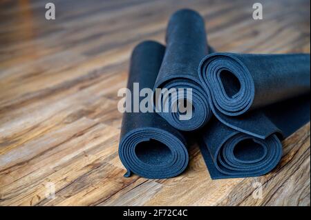 Mehrere gerollte Yoga- oder Fitness-Gummimatten in schwarzer Farbe auf Holzboden. Sport-Accessoires Stockfoto