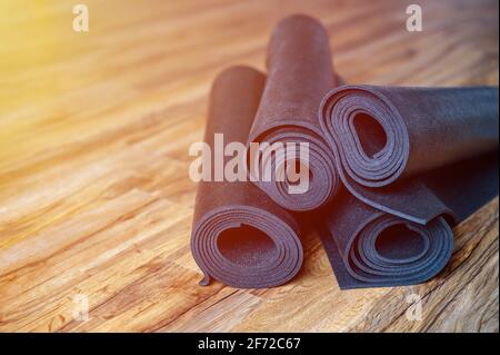 Mehrere gerollte Yoga- oder Fitness-Gummimatten in schwarzer Farbe auf Holzboden. Sport-Accessoires. Flare Stockfoto