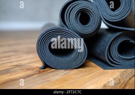 Mehrere gerollte Yoga- oder Fitness-Gummimatten in schwarzer Farbe auf Holzboden. Sport-Accessoires Stockfoto