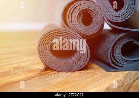 Mehrere gerollte Yoga- oder Fitness-Gummimatten in schwarzer Farbe auf Holzboden. Sport-Accessoires. Flare Stockfoto