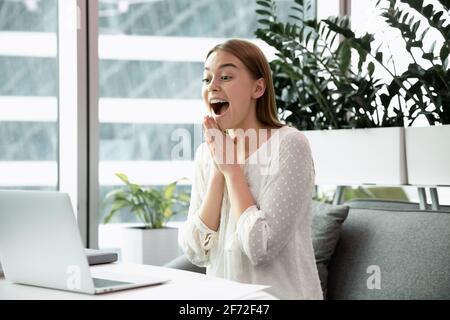 Aufgeregte weibliche Angestellte triumphieren beim Lesen der Nachrichten auf dem Laptop Stockfoto