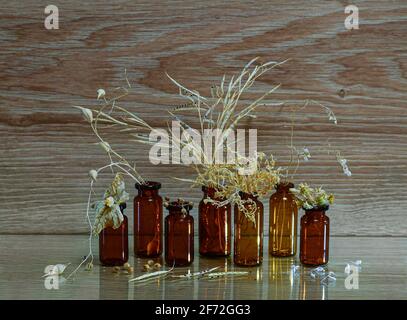 Dunkle Glasflaschen mit getrockneten Kräutern von hellgelber Strohfarbe mit Samen in Schachteln und Blumen. Auf einem hölzernen Hintergrund. Stockfoto