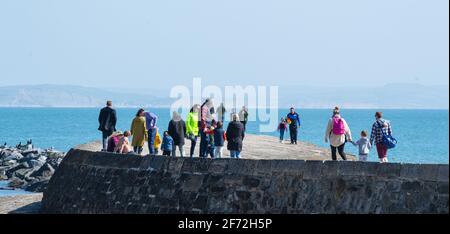 Lyme Regis, Dorset, Großbritannien. April 2021. Wetter in Großbritannien. Ostersonntag: Am Ostersonntag strömen Massen an den malerischen Strand am Badeort Lyme Regis, um das Beste aus der milden Sonne und dem blauen Himmel zu machen. Die Menschen flanieren entlang der Cobb-Mauer. Kredit: Celia McMahon/Alamy Live Nachrichten Stockfoto