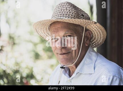 Porträt eines älteren lächelnden Mannes mit Strohhut, der auf die Kamera schaute. Ältere Menschen Lebensstil, Abend Glühfilter. Stockfoto