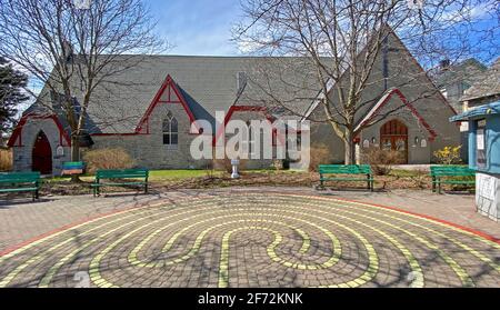 Alte Steinkirche mit roten Zierleisten - grüne Parkbänke - ein 7-schichtiger Labyrinthweg im Innenhof Stockfoto