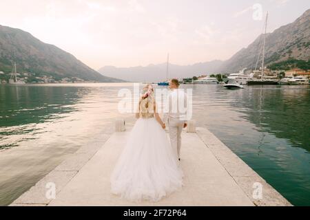 Die Braut in einem Kranz und Bräutigam gehen entlang der pier hält Hände in der Nähe der Altstadt von Kotor in Die Bucht von Kotor Stockfoto