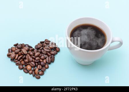 Dampfende Kaffeetasse, herzförmige Kaffeebohnen auf blauem Hintergrund, Platz zum Kopieren. Morgenkaffee für die Liebsten. Stockfoto
