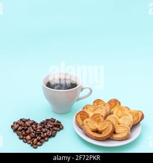 Dampfende Kaffeetasse, herzförmige Kekse, herzförmige Kaffeebohnen auf blauem Hintergrund, Kopierfläche, quadratische Form. Frühstück am Morgen. Frühstück für Stockfoto