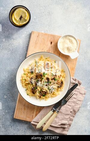 Speisen italienische Pasta-Risoni, Pilze, Sauce, Parmesan, Thymian, Knoblauch, Olivenöl, in weißer Platte auf Schiefer, Stein oder Beton Hintergrund. Draufsicht w Stockfoto