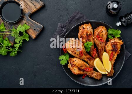 Gegrillte Hähnchenschenkel oder gebratene grillgerichte mit Gewürzen und Tomatensalsa-Sauce auf einem schwarzen Teller. Draufsicht mit Kopierbereich. Stockfoto