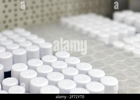 Zylindrische Kunststoffgläser mit runden Verschlüssen für Nahrungsergänzungsmittel oder Lebensmittel. Weiße, opake Behälter in rohen Roh-Regalen für die Pharmaindustrie. Bereit t Stockfoto