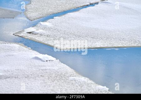 Rissene Eis des gefrorenen Flusses mit weißem Schnee oben und blauem Wasser unten. Hintergrund mit Eisstruktur, Nahaufnahme. Stockfoto