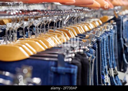 Reihe von aufgehängten blauen und schwarzen Jeans auf hölzernen Kleiderbügeln im Laden. Viele Jeans hängen auf dem Regal. Reihe von Hosen Denim Jeans hängen im Schrank. Kaufkonzept, Stockfoto