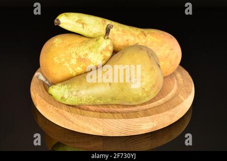 Vier Bio-frische, saftig-süße Konferenzbirnen auf einem runden Bambustablett. Der Hintergrund ist schwarz. Stockfoto