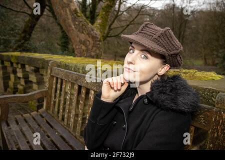 Eine attraktive junge Frau in einem öffentlichen Park saß darauf Eine alte Bank an einem kalten Tag im Winter Die Zeit schaut glücklich und lächelt Stockfoto