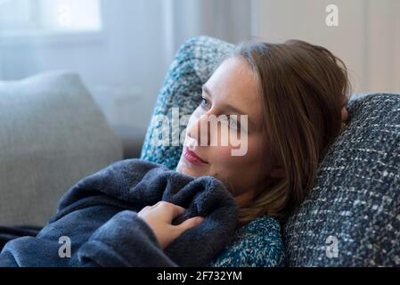 Eine junge Frau liegt in Dorfen, Bayern, auf einem Sofa in einer Decke gekuschelt Stockfoto