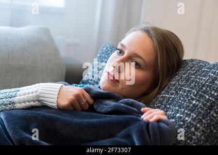 Eine junge Frau liegt in Dorfen, Bayern, auf einem Sofa in einer Decke gekuschelt Stockfoto