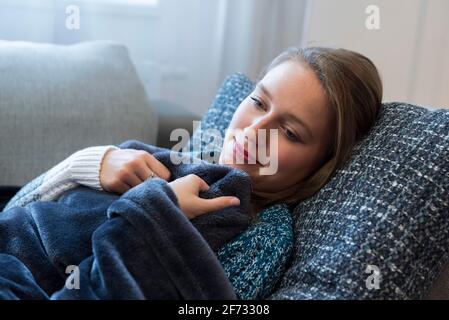 Eine junge Frau liegt in Dorfen, Bayern, auf einem Sofa in einer Decke gekuschelt Stockfoto