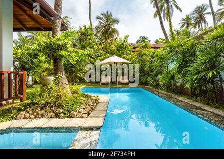 Pool mit Sonnenschirm und Strandliegen im tropischen Hotel oder Ferienhaus. Schöner Pool im Innenhof des Wohnhauses. Landschaftsdesign von b Stockfoto