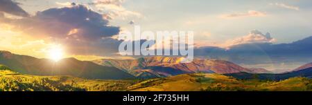 Bergige ländliche Panoramalandschaft im Frühling bei Sonnenuntergang. Wunderschöne Landschaft unter einem Himmel mit Wolken im Abendlicht. Grasbedeckter Hügel rollt Stockfoto