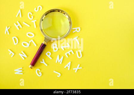 Lupe auf gelbem Hintergrund mit verstreuten Buchstaben des Alphabets Stockfoto