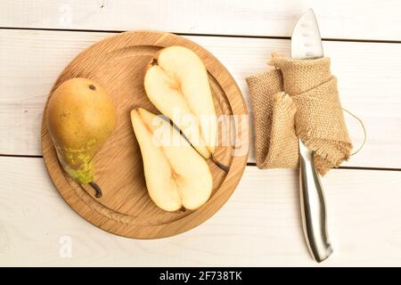 Eine ganze und zwei Hälften von Bio frisch saftig süß lecker Konferenz Birnen auf einem Bambustablett mit einem Metallmesser mit einer Jute Serviette, auf einem Tisch gemacht o Stockfoto