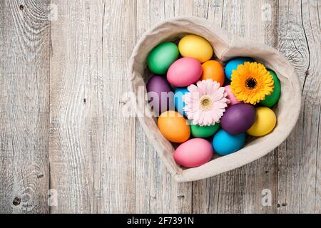 Ostereier und Gerbera-Blüten im herzförmigen Korb Stockfoto