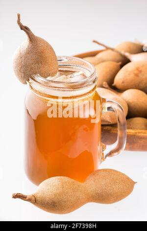 Tamarindensaft in einem Glas, umgeben von frischen reifen Tamarinden - Tamarindus indica Stockfoto