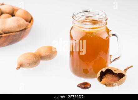 Tamarindensaft in einem Glas, umgeben von frischen reifen Tamarinden - Tamarindus indica Stockfoto