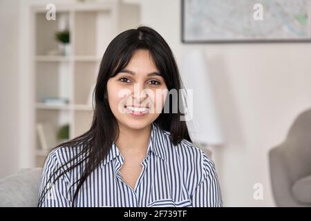 Porträt einer jungen glücklichen indischen Frau, die im Heimbüro auf die Kamera schaut. Stockfoto