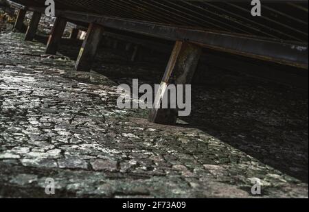 Eine moosige, grünliche Steinstruktur unter einem Pier Ebbe bedeckt mit einer Kruste getrockneter Algen mit Metallsäulen, die die Böschung und unterstützen Stockfoto