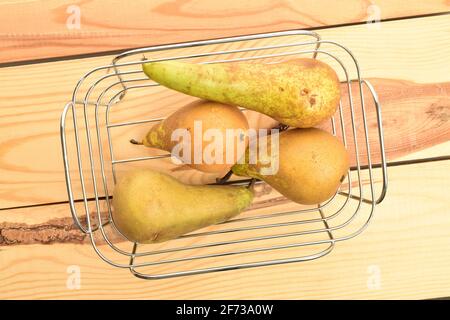 Gruppe von vier reifen Bio süß lecker Konferenz Birnen mit einem Korb aus Metalldraht, auf einem Tisch aus Holz. Stockfoto