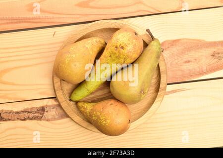 Eine Gruppe von vier reifen Bio-süßen Tasty Conference Birnen auf einem runden Bambustablett, auf einem Tisch aus Holz. Stockfoto