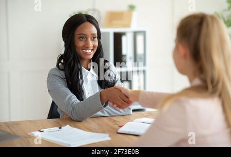 Nicht erkennbarer schwarzer HR-Manager schüttelt sich die Hände mit weiblicher Arbeitsuneifer Zum Vorstellungsgespräch im Büro Stockfoto