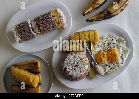 Gedämpfter Hirsemehlkuchen mit einer großzügigen Schicht frischer Kokosnuss dazwischen. Lokal bekannt als Ragi puttu. Serviert mit gedämpftem Kochbananen und Friese Stockfoto