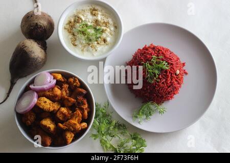 Rote Beete Pulao, ein ein-Topf-Reiszubereitung mit Basmati-Reis, Rote Beete, Zwiebeln und Gewürzen. Serviert mit luftgebratenen Hähnchenbissen und Quark. Auf Weiß geschossen Stockfoto