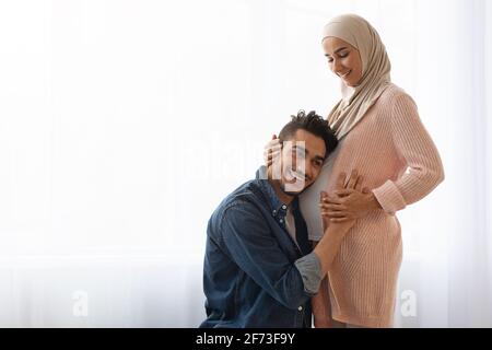 Frohe Erwartungen. Liebevoller arabischer Ehemann Höllenanhörung des Bäuers seiner schwanger-muslimischen Frau Stockfoto