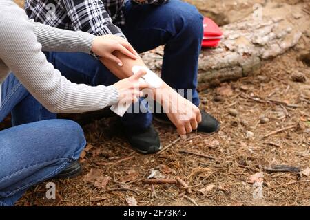 Junge Frau, die den verletzten Arm eines reifen Mannes im Wald desinfiziert Stockfoto