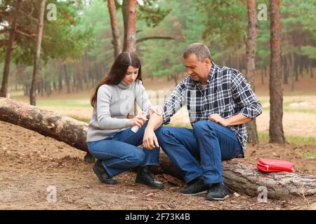 Junge Frau, die den verletzten Arm eines reifen Mannes im Wald desinfiziert Stockfoto