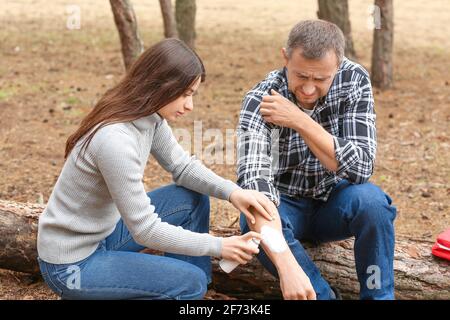 Junge Frau, die den verletzten Arm eines reifen Mannes im Wald desinfiziert Stockfoto