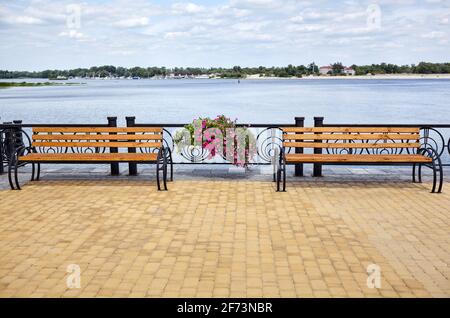 Böschung mit Bänken mit Blick auf das Meer. Parken Sie die Holzbank auf dem gepflasterten Bürgersteig Stockfoto