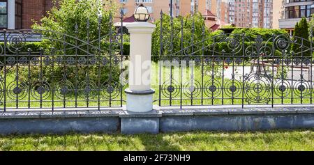 Schmiedeeiserner Zaun. Bild von einem schönen dekorativen gusseisernen schmiedeeisernen Zaun mit künstlerischen Schmieden und Steinsäulen Stockfoto