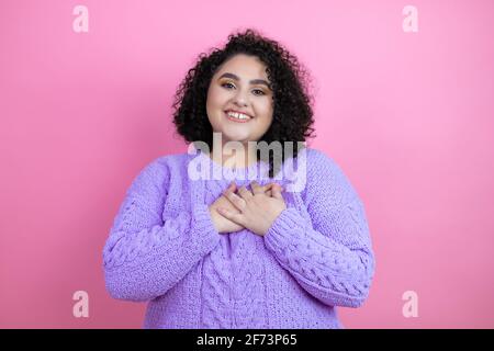 Junge schöne Frau trägt lässigen Pullover über isolierten rosa Hintergrund lächelt mit ihren Händen auf der Brust und dankbare Geste auf ihrem Gesicht.