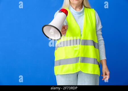 Reife Frau in Weste und mit Megaphon auf farbigem Hintergrund Stockfoto