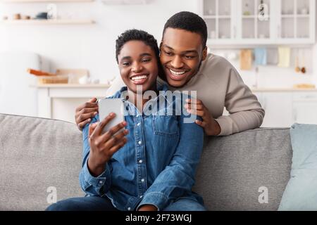 Schwarzes Paar sitzt auf der Couch, mit Smartphone Stockfoto