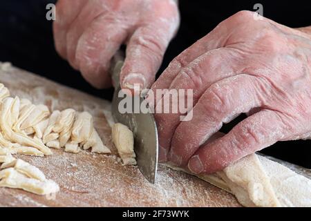 Nahaufnahme eines Senioren Hände schneiden Eiernudeln Stockfoto