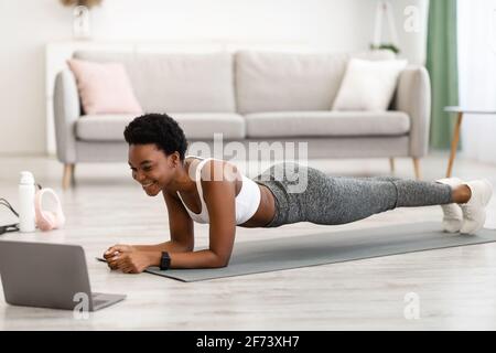 Sportliche Afrikanische Hündin Beim Laptop-Training Im Plank Indoor-Bereich Stockfoto