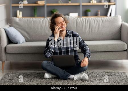 Kerl Im Gespräch Auf Smartphone Sitzen Mit Laptop Auf Dem Boden Indoor Stockfoto