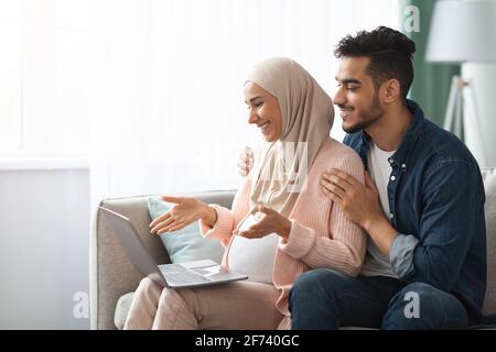 Fröhlich Schwanger Islamischen Ehegatten Mit Laptop Macht Video-Anruf Bei Zu Hause Stockfoto